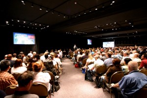 transmit pre-planned content: photograph of a large conference hall with attendees sitting in rows and listening to a distant speaker. Image attribution: http://www.flickr.com/photos/plakboek/ / CC BY-NC-ND 2.0