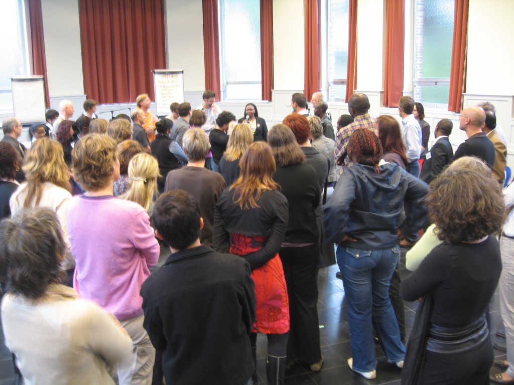 Participation techniques you can use in conference sessions: photograph of a large crowd of conference attendees standing facing a speaker with many flipcharts behind her. Photo attribution: Flickr user choconancy.