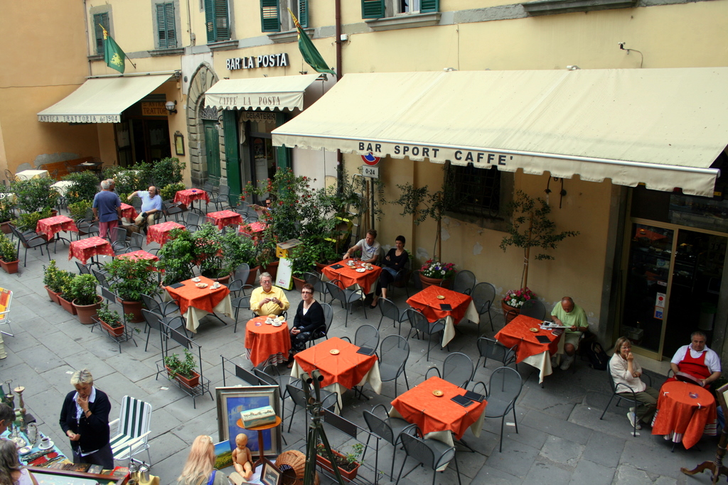 event tourists: a Tuscany outdoor cafe with patrons sitting at tables with orange tablecloths. Image attribution: Flickr user decadence