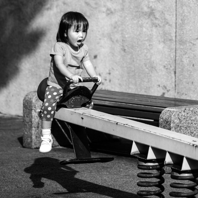 Give attendees experiences not things: a black-and-white photograph of a child with her mouth open in excitement, on the end of a seesaw. Photo attribution: Flickr user shahiran83