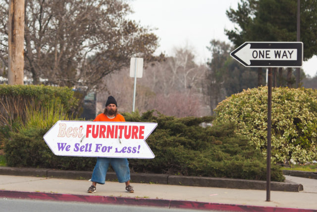 next best thing: photograph of a street with a ONE WAY sign. A man on the sidewalk is carrying a large arrow-shaped sign that says
"Best FURNITURE
We Sell For Less!"