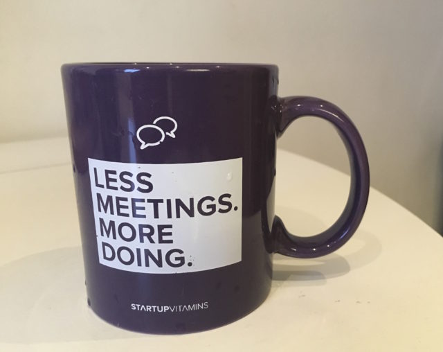 Photograph of a purple mug with the slogan "less meetings more doing"