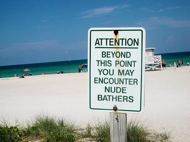 How to get attendees to risk doing something new at your event: a photograph of a sign on a beach that says
"ATTENTION
BEYOND THIS POINT YOU MAY ENCOUNTER NUDE BATHERS"