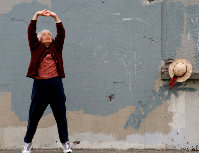 Stretching the mind: A standing woman does a stretch with her hands clasped above her head. Photo attribution: Flickr user glenscott