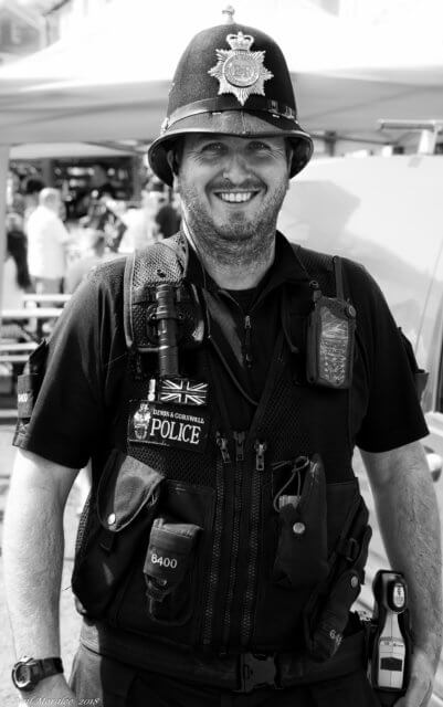 Develop products and services with clients at conferences: a black-and-white photograph of a smiling British police officer wearing a helmet and multiple items of equipment around his body