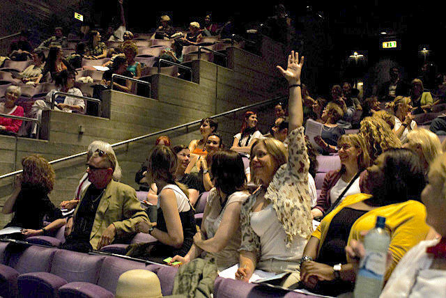 Any questions? Rethinking traditional Q&A. A woman, seated in the midst of an audience, raises her hand.