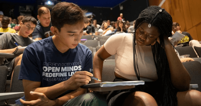 switching to active learning: a photograph of two students sitting next to each other in a classroom looking at a set of notes together. Image attribution: Inside Higher Ed & Kris Snibbe / Harvard University