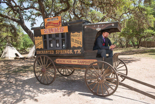 NFTs event marketing: photograph of a snake-oil salesman sitting at the front of a "wild-west" stagecoach covered with advertisements