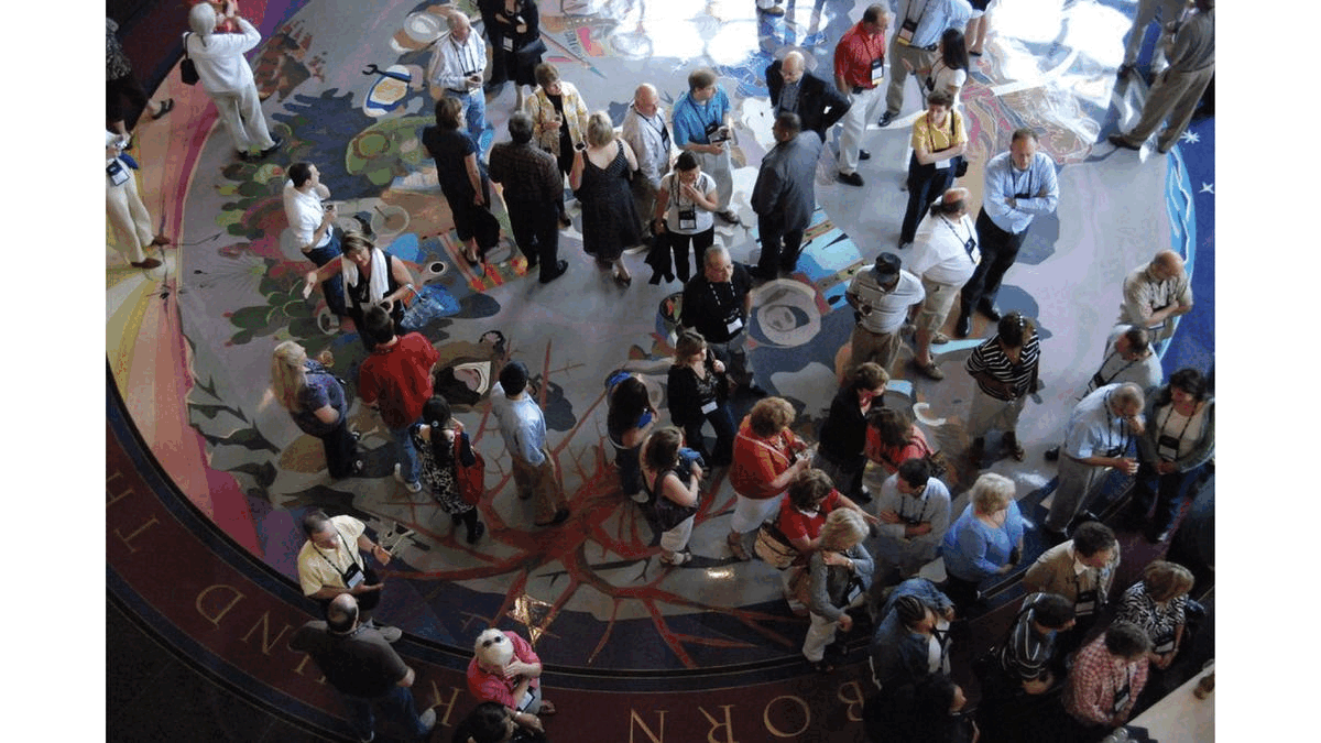 hear me! Photograph taken from above of a conversing crowd. An ignored facilitator stands in the center. Image attribution: "2010 IACA Conference - evening reception at the Bob Bullock Texas State History Museum" by Corvair Owner is licensed with CC BY-SA 2.0. and modified with additional graphics.