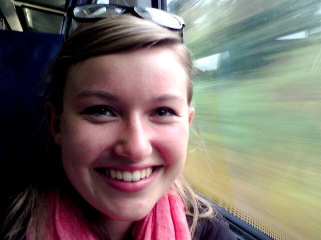 A smiling woman, full of nervous excitement, sits on a train with the blurred world speeding past her window.