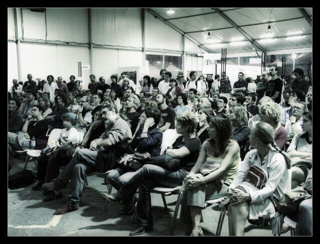 Social listening: A black and white photograph of a hall containing a seated audience listening to something happening in front of them.