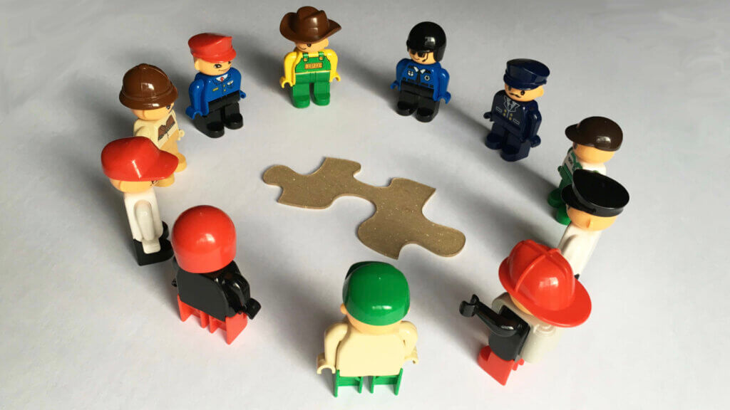 Solve problems together: a photograph of a circle of standing Lego people surrounding a jigsaw puzzle piece Image attribution: Wikimedia Commons under the Creative Commons Attribution-Share Alike 4.0 International license