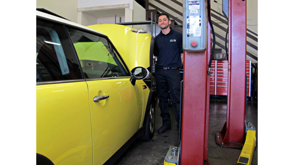 The importance of trust: photograph of a smiling mechanic standing beside a bright yellow Mini in his garage Image attribution: Flickr user Bennilover